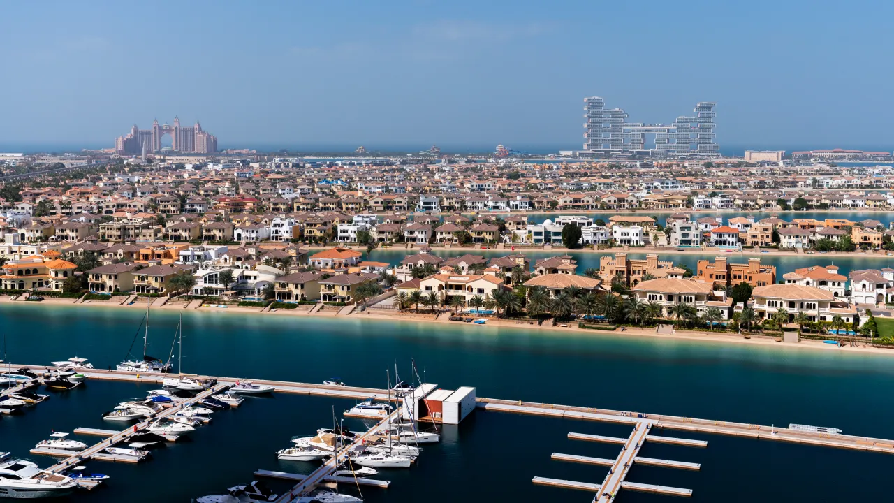 Aerial view of Palm Jumeirah — waterfront villas, a marina full of yachts, and Atlantis on the horizon